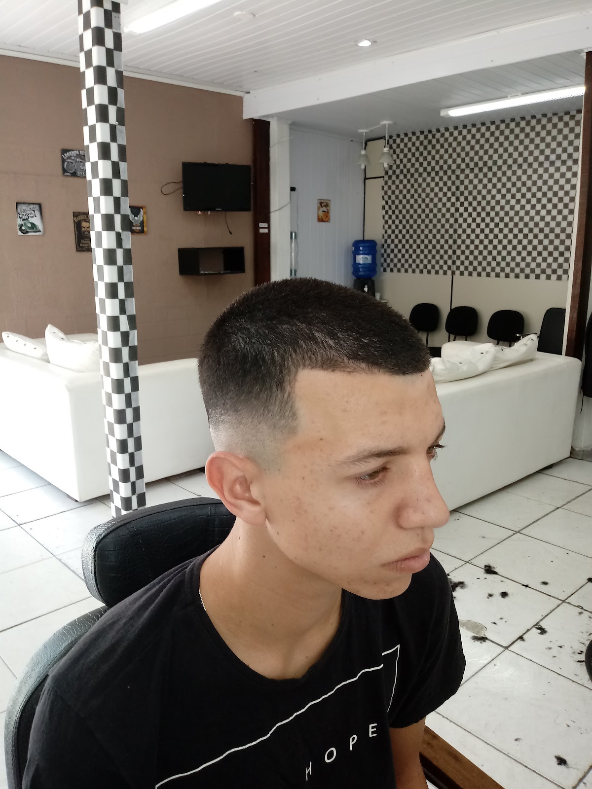 Corte de cabelo finalizado, com a parede xadrez da Barbearia Ponto 47 ao fundo